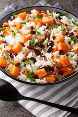 Vegetarian pilaf with sweet potato, basmati, nuts, onions and dried cranberries close-up in a bowl on the table. Vertical