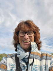 Mature woman takes a selfie for social media or a family messaging group. She is walking along Rhossili Bay on the Gower Peninsular in autumn and wearing casual clothing.