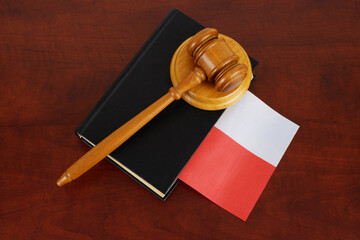Wooden judge gavel and legal book with flag of Poland on wooden table.