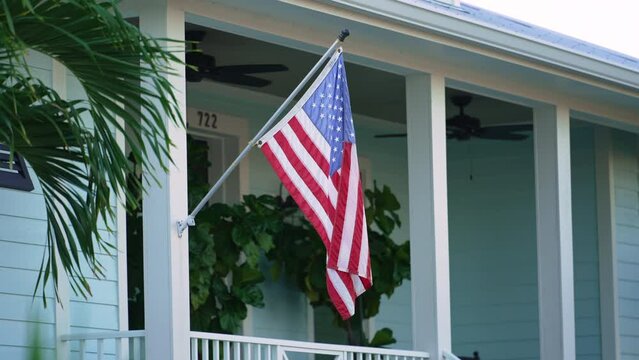 Florida suburban home with USA national flag waving on wind in front yard. American stars and stripes spangled banner as symbol of democracy