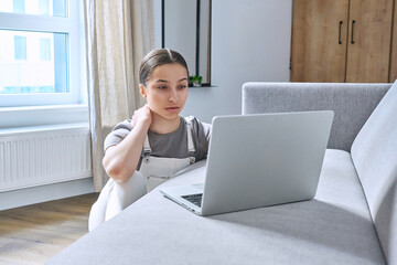 Teen girl at home on couch using laptop