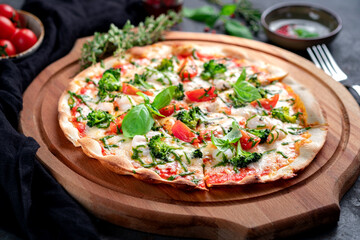 Classic pizza with herbs, broccoli, tomatoes, basil and pesto sauce on a thin dough.