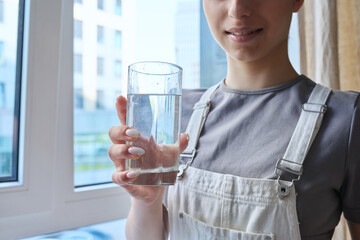 Close-up of teenage girl drinking water from glass, at home