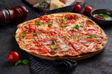 Spicy meat pizza on a dark background. Pizza with sausage, chicken and hot sauce with pepper and tomatoes. Close-up