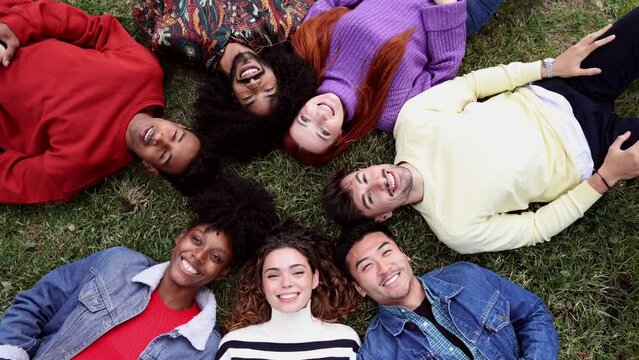 A diverse group of friends are lying on a grass in a circle with their heads together and hands in the air. no to racism. solidarity