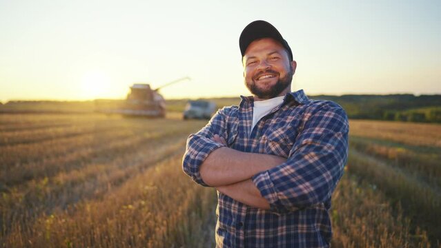 Portrait happy farmer manager man with tablet works controls wheat harvesting on farm field, collecting data at sunset. Farm worker engineer. Harvesting time, farming, collecting ripe crop concept.