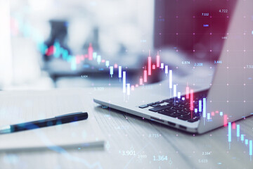 Close up of laptop on office desk with supplies and glowing downward candlestick forex chart on blurry background. Crisis, financial loss and crash concept. Double exposure.