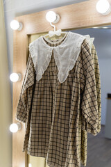 Dress with a white collar in a fitting room with a large mirror. Beige checkered dress for girls. Children's clothing store. Sale in a children's clothing store. Vertical photo.