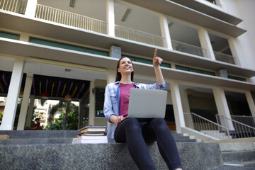 Young woman working with laptop while sitting on the stairs of the university building.