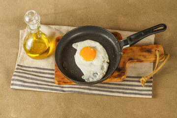 fried egg with extra virgin olive oil in a frying pan with a glass bottle with oil on a wooden board