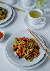 green spinach pasta with vegetables in the white plate on white background with tea
