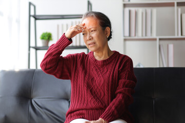 Senior woman sitting on the sofa at home is sick and has a headache.