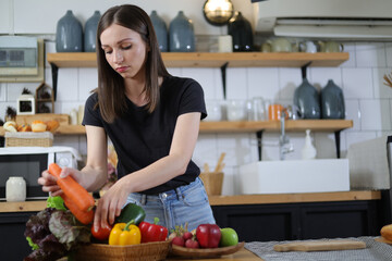 Attractive young woman in the kitchen choosing vegetables in a basket.
