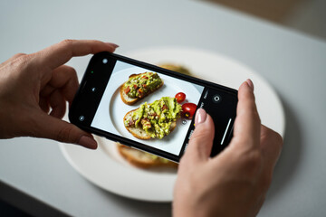 Close-up of a woman's hand photographing a fresh breakfast with a smartphone. 