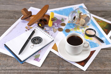 A white cup of coffee on the wooden background is next to world maps, compass, magnifier, ...