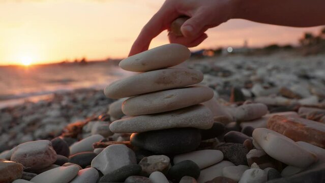 The hand of a mother and a child build a pyramid from pebbles on the sea beach during sunset. construction and planning concept. High quality 4k footage