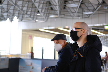 two men in medical mask waiting for the plane to arrive at the airport, travelling during covid-19...