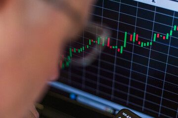 Close up shot of the mid aged man next to the computer screen with trading bar charts. Finance