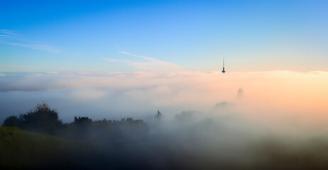 Auckland Sky Tower above a sea of fog. View from Mt Eden summit with the volcanic crater in...