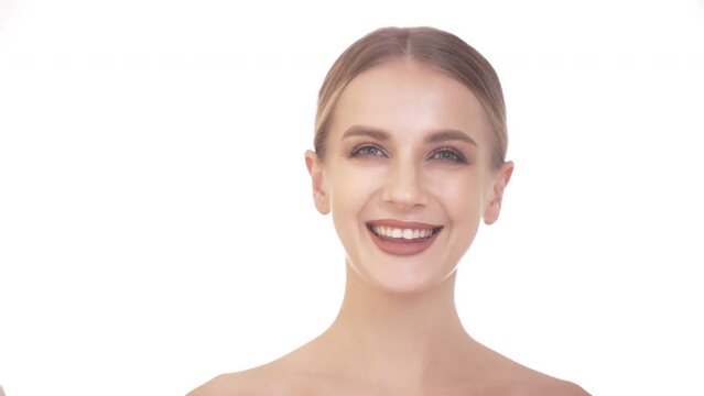 A young joyful woman with clean skin wipes her face with a cotton pad. White background.