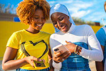 Muslim african woman and afro friends using mobile phone outdoors