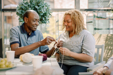 Smiling female nurse assisting senior man in crocheting at nursing home
