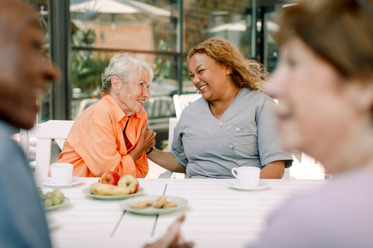 Cheerful young female caregiver sitting with retired senior man and women at dining table