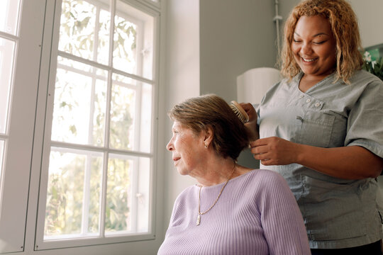 Low angle view of young female nurse brushing senior woman's hair at retirement home