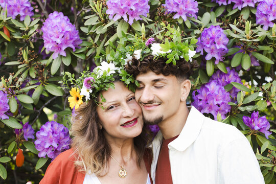 Smiling mother and son wearing tiaras against flower plants at back yard during Swedish summer solstice