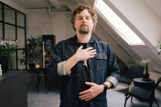 Businessman with eyes closed and hand on chest standing at office