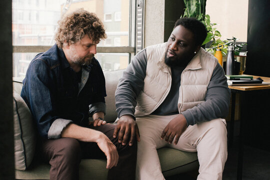 Businessman consoling with colleague while sitting on sofa at office