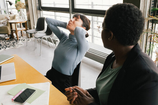 Businesswoman sitting besides overworked female colleague struggling with pain at office