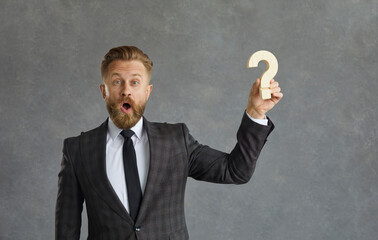 Businessman finds answer and business solution. Portrait of happy funny looking curious bearded man in suit with surprised face expression holding question mark standing isolated on grey background - obrazy, fototapety, plakaty