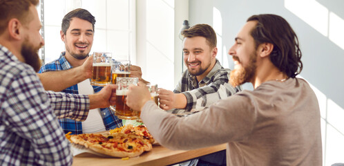 Group of happy, cheerful young men having a party, sitting at table, drinking beer, saying toasts, clinking mugs, eating tasty pizza, and having fun together. Friends, leisure, fun concepts. Banner
