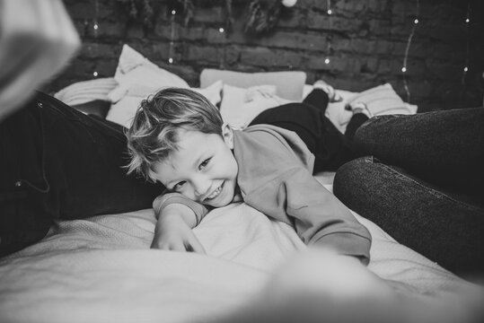 Child lying on bed. Concept of family holiday. Father, mother hug son at home. Happy New Year and Merry Christmas. Mom, dad embrace kid. Christmas tree, decorated interior. Black and white photo