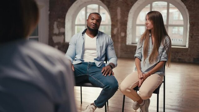 A fit man with Black skin in a blue shirt and a girl with long hair communicate with a psychologist during group therapy