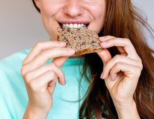 Young female person eating healthy food, biting multigrain bread close-up.