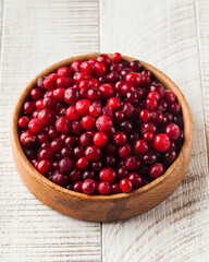 Juicy fresh cranberries in a wooden bowl on a white wooden background. Berries.