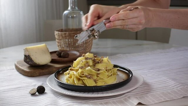 Serve the black truffle with a slicer on a plate of fettuccine mushrooms pasta, long egg pasta with cheese. Italian first course, home interior.