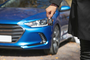 Woman showing car key against the background of a car.