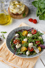 salad with green leaves and tomatoes and cream cheese, a glass bottle with olive oil next to it, a bowl with tomatoes and basil leaves
leaf salad, lettuce
