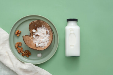 The green ceramic plate holds walnuts and shredded fresh coconut. Next to it is a bottle of white nut milk. Nut milk contains abundant nutrients that are beneficial to the body.