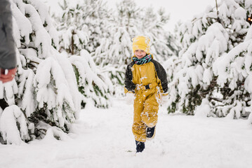 Baby boy playing snow among snowdrifts closeup. Little child in winter clothes having fun. Kid wearing warm hat walking in winter park in holidays. Toddler in mountain country in snowy forest.