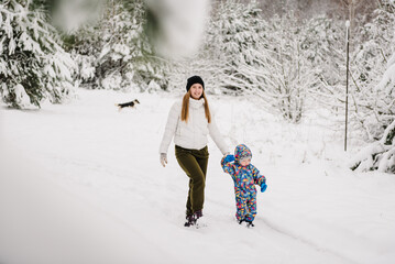 Mother holds hand little baby son having fun walking in snow nature. Happy mom and child playing in winter park, spending holidays. Family walk in mountain country in snowy forest together. Closeup