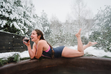 Woman drink cool drinks and relax in hot bath outdoors. Female enjoying thermal spa snowy forest....