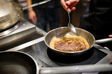 Professional chef cooking beef steak in frying pan on stove in restaurant kitchen