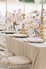 Close-up of fragment of wedding table in beige tones of with bouquets of roses, candlesticks.