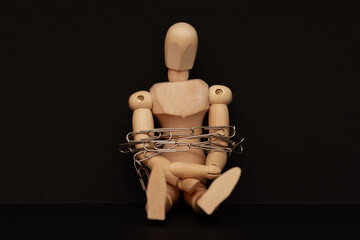 Wooden mannequin sitting on black background tied with paper clips, concept of office slavery,...