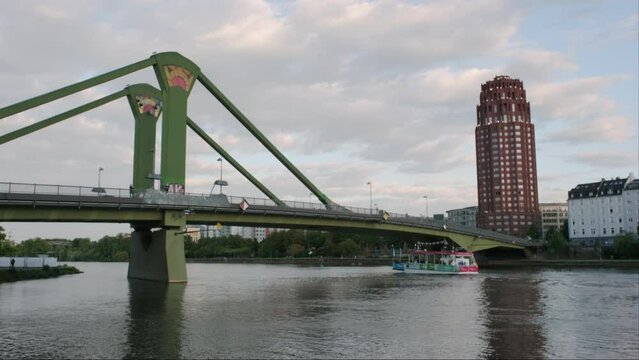 River Main tour boat passes under Floserbrucke bridge on a summer evening in Frankfurt. The Lindner Hotel is seen behind