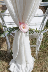 White light chair decorated with white fabric, fresh flowers is prepared for wedding ceremony. 